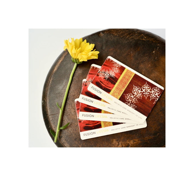 A yellow flower and a stack of four gift cards resting on a small wooden table. 